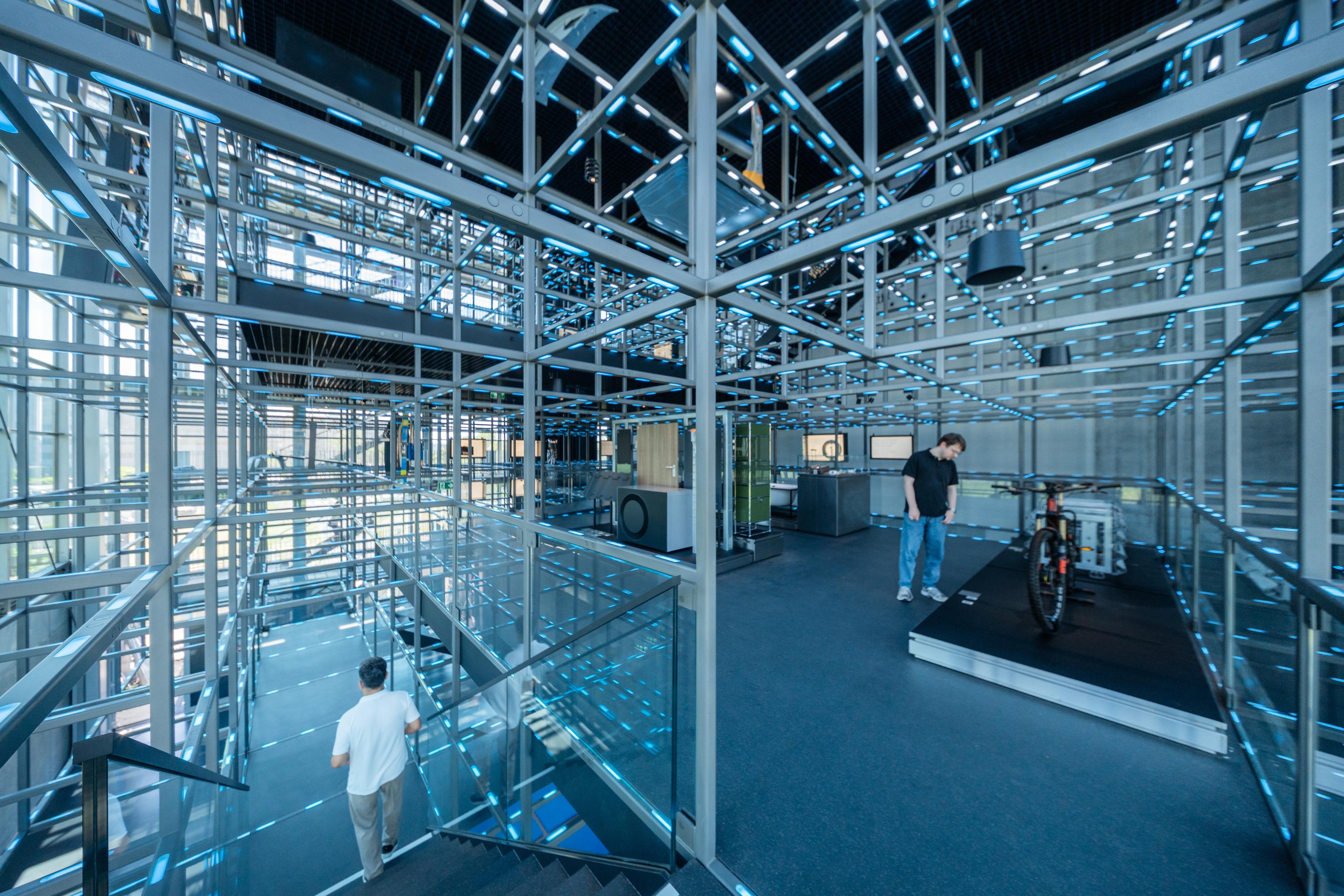 Visitors explore the illuminated steel framework of the voestalpine Stahlwelt exhibition. The multi-level “Grid” structure, composed of steel beams and integrated LED lighting, creates a walkable spatial landscape that showcases steel applications and technological innovations across different industries